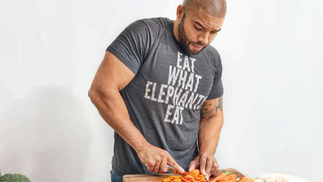 dom-image-option-2 Dom Thompson chops carrots and wears a shirt that says Eat What Elephants Eat