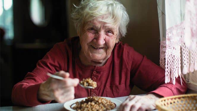 Frailty in Older Women Old woman in red sweater eats a bowl of grains and smiles at the camera
