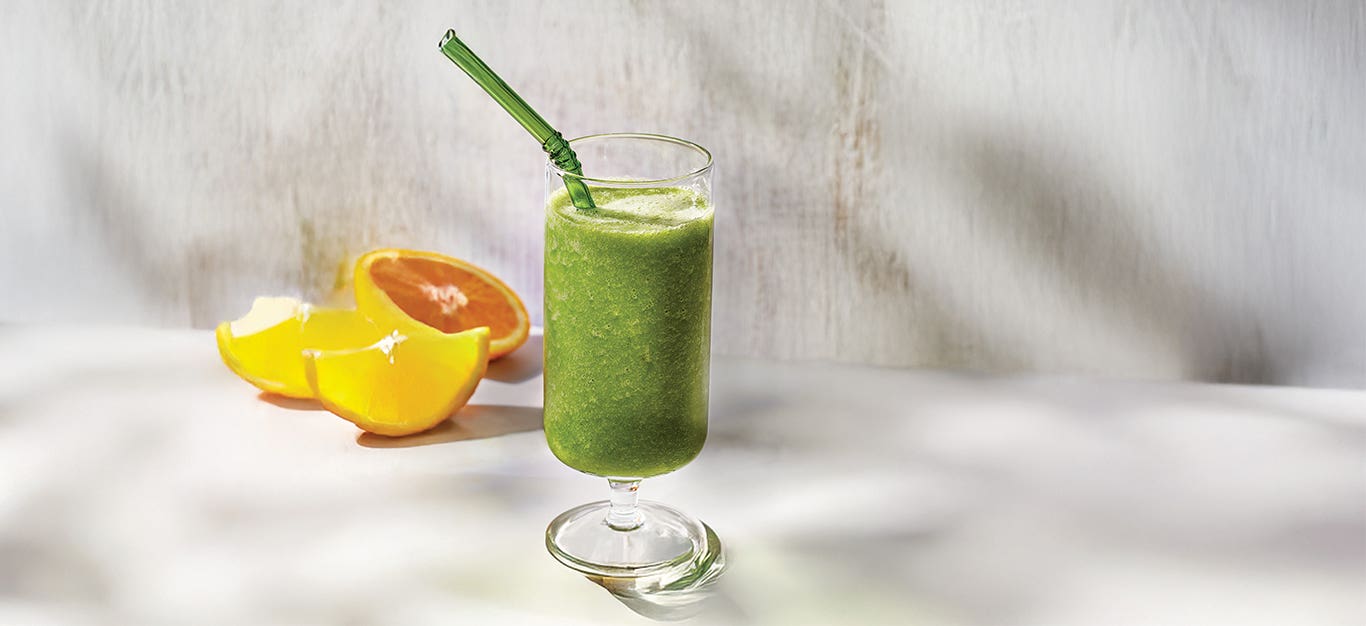 Kale Apple Smoothie in a wine glass with cut orange halves behind