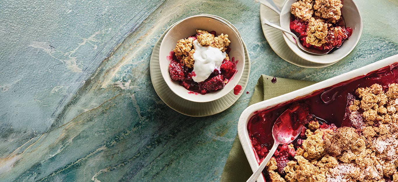 Not-Picky Fruit Crisp in a white casserole dish with one serving in a white bowl, topped with Aquafaba Whipped Cream