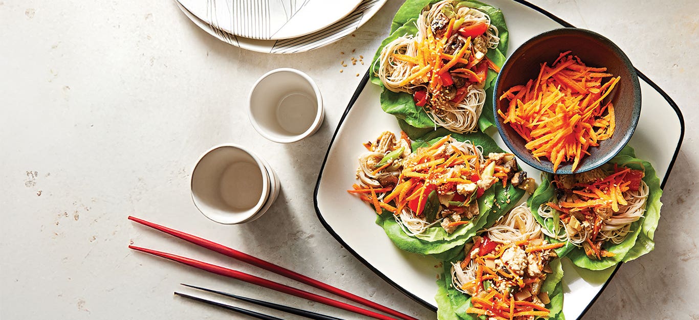 A square white plate of four Tofu Lettuce Wraps next to two sets of chopsticks.